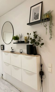 there is a white dresser with plants on top and a mirror hanging above the drawers