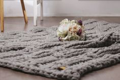 a bouquet of flowers is sitting on the floor next to a gray knitted blanket