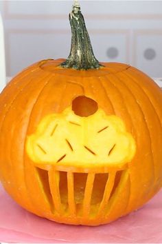 a pumpkin carved to look like it has a face on it's side and is sitting on a pink surface