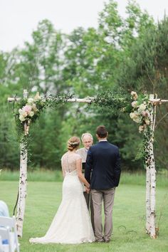 a bride and groom standing under an arch made from birch trees at the end of their wedding ceremony