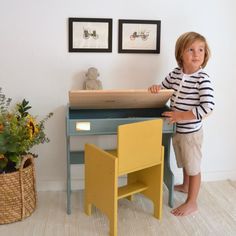 a little boy that is sitting at a desk with a book in his hand and some flowers