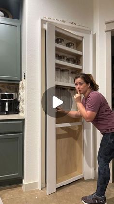 a woman standing in front of an open pantry door and holding the door to another cabinet