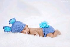 a baby wearing a blue knitted hat and diaper is laying on white fur