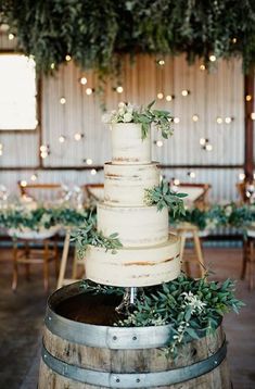 a wedding cake sitting on top of a wooden barrel in front of tables and chairs