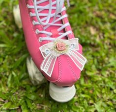 a pink roller skate with white laces and a flower on the side, sitting in grass