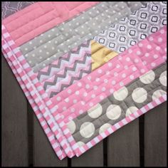 a close up of a pink and gray quilt on a wooden table with polka dots