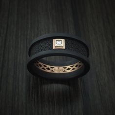 two black rings with gold accents and a diamond in the center on a wooden surface