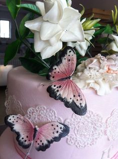 there is a pink cake with butterflies on it and white flowers in the back ground