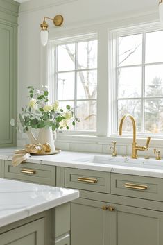 a kitchen with green cabinets and white counter tops, gold faucets and brass handles