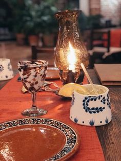 a table topped with plates and glasses filled with liquid next to a lit candle on top of a wooden table