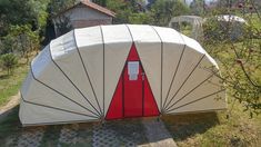 a white and red tent sitting on top of a grass covered field next to trees