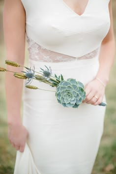 a woman in a white dress holding a succulent and flower bouquet on her wedding day