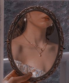 a woman's reflection in a round mirror with pearls on the chain around her neck