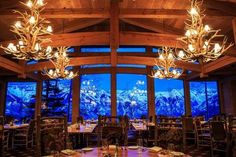 a dining room with large windows overlooking the mountains and snow covered peaks is lit by chandeliers