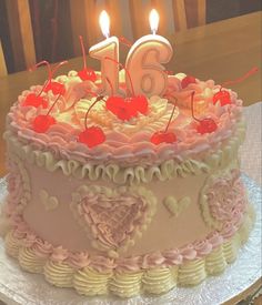 a birthday cake with pink frosting and hearts on it, lit by two candles