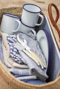 a basket filled with dishes and cups sitting on top of a beach