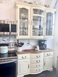 a kitchen with white cupboards and glass front cabinets on the wall, along with a black stove top oven