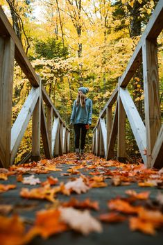 a woman walking across a wooden bridge surrounded by leaves