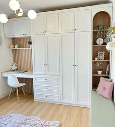 a bedroom with white cabinets and pink pillows on the floor next to a desk in front of a bookcase