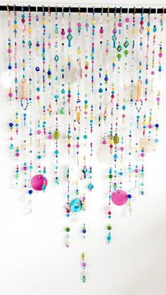 a white wall with beads hanging from it's side and a pink object in the middle