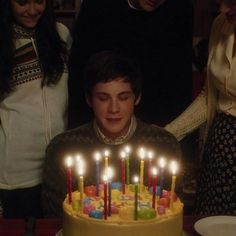 a man sitting in front of a birthday cake with lit candles on top of it