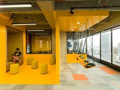 a man sitting on a bench in an office with yellow walls and floor to ceiling windows