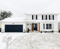 a white house with black shutters and snow on the ground in front of it