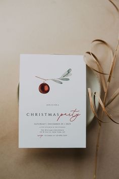 a christmas party card sitting on top of a white plate next to a brown ribbon