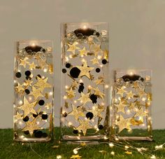 three clear glass vases with gold stars and lights in them sitting on the grass