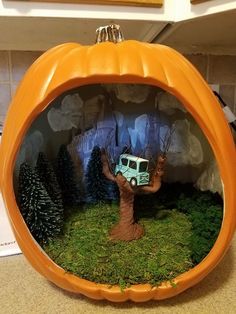 an orange pumpkin shaped container filled with fake trees and a toy truck in the center