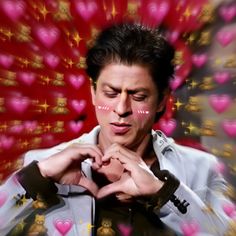 a man making a heart shape with his hands while standing in front of pink hearts