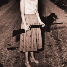 an old photo of a woman holding a bat and a dog on the side of the road