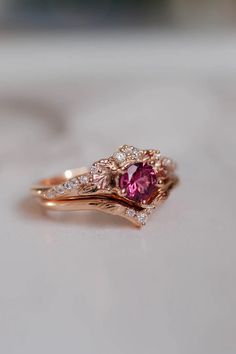 a close up of a ring with a pink stone in the middle and two diamonds on top