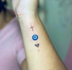 a woman's wrist with a cross and evil eye tattoo on the left arm