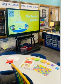 a classroom with tables, chairs and a flat screen tv on the wall that says the secret stories