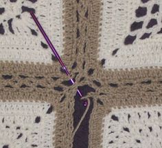 a crocheted blanket with a purple needle in the center and white squares on it