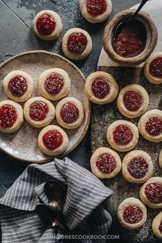 small cookies with jam on them are sitting on a plate next to a bowl and spoon