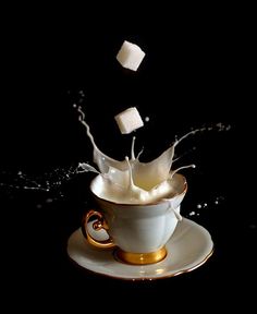 a cup filled with milk splashing out of it on top of a saucer