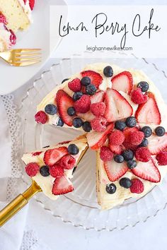 a cake with berries and blueberries is on a white plate next to a gold fork