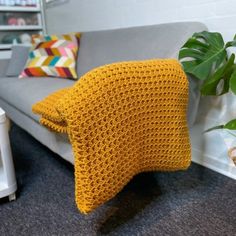 a yellow knitted pillow sitting on top of a couch next to a potted plant