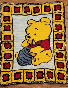 a crocheted winnie the pooh blanket on a wooden floor with a teddy bear holding a honey pot