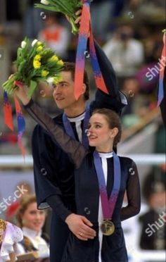 a man and woman standing next to each other with medals around their necks, both holding flowers