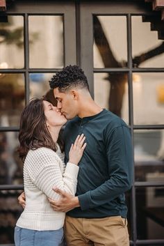 a man and woman are kissing in front of a glass door with their arms around each other