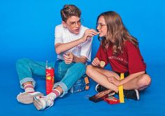 two young people sitting on the ground eating snacks and condiments with toothbrushes