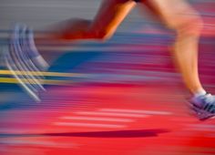 a blurry photo of a person running on a track with the colors of red, white and blue