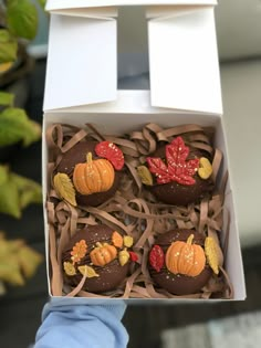 someone holding up a box of chocolates decorated with leaves and pumpkins