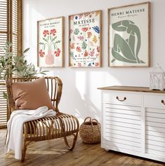 three framed art prints hang on the wall next to a chair and sideboard in a white room