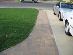 two cars parked on the side of a road next to a grass covered driveway and sidewalk