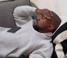 a man laying on top of a couch with his head in his hands while looking at something