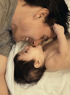 a man kisses his baby's forehead while laying in bed